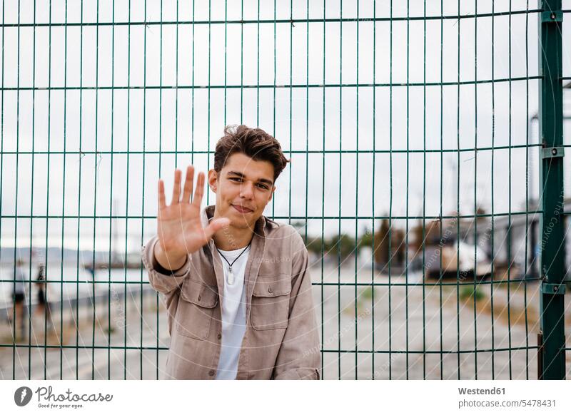 Hübscher junger Mann zeigt Hand gegen Metallzaun Farbaufnahme Farbe Farbfoto Farbphoto Portugal Außenaufnahme außen draußen im Freien Tag Tageslichtaufnahme