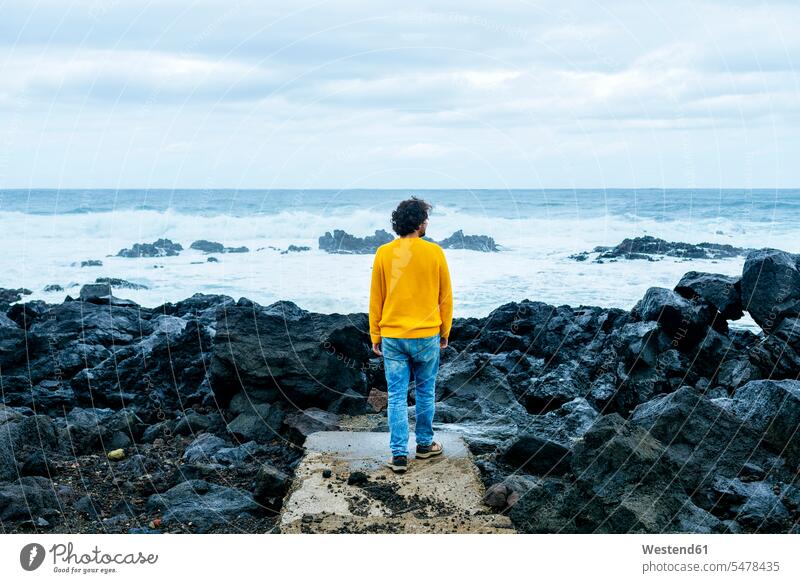 Azoren, Sao Miguel, Rückansicht eines Mannes, der von der steinigen Küste auf das Meer schaut Männer männlich Meere stehen stehend steht Kueste Kuesten Küsten