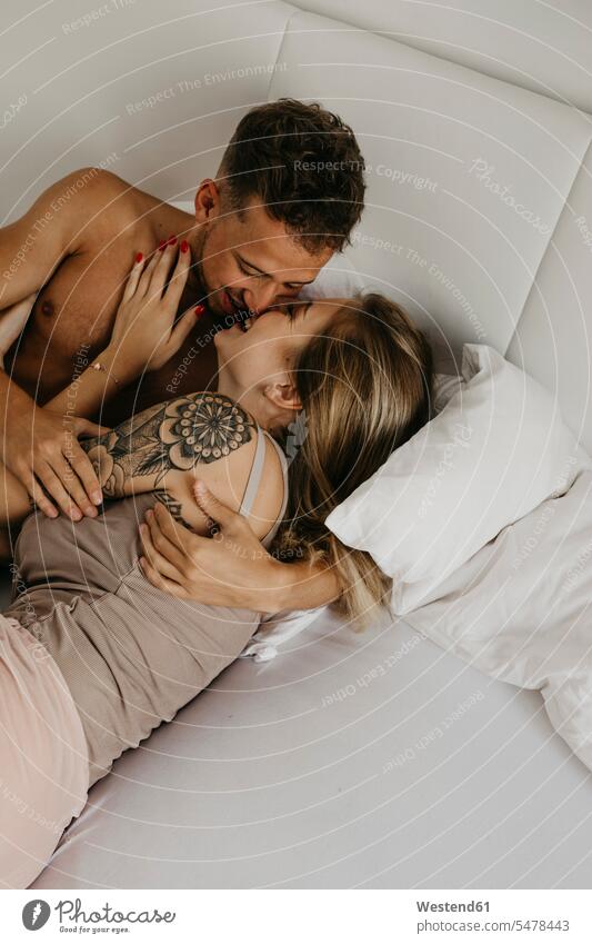 Glückliches junges Paar, das sich im Bett küsst liegen liegend liegt Betten küssen Küsse Kuss glücklich glücklich sein glücklichsein Pärchen Paare Partnerschaft