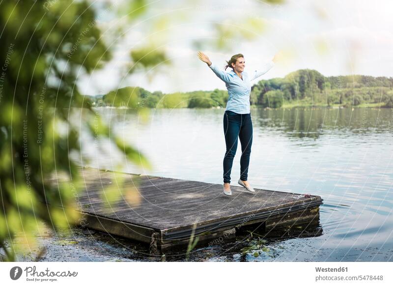 Frau macht einen Hampelmann auf einem Steg an einem See Stege Anlegestelle Seen weiblich Frauen Gewässer Wasser Erwachsener erwachsen Mensch Menschen Leute