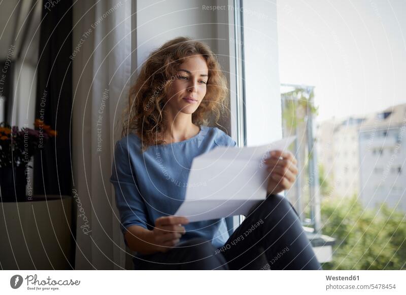 Frau liest Zeitung, während sie zu Hause auf dem Fensterbrett sitzt Farbaufnahme Farbe Farbfoto Farbphoto Innenaufnahme Innenaufnahmen innen drinnen Tag