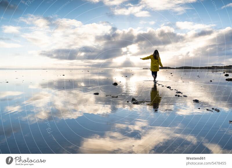 Frau beim Spaziergang mitten im Meer mit Reflexion am Strand des Hvalnes-Naturreservats, Island Farbaufnahme Farbe Farbfoto Farbphoto Außenaufnahme außen