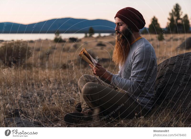 USA, Nordkalifornien, bärtiger junger Mann liest ein Buch in der Nähe des Lassen Volcanic National Park Bücher lesen Lektüre Bart Bärte Männer männlich Mensch