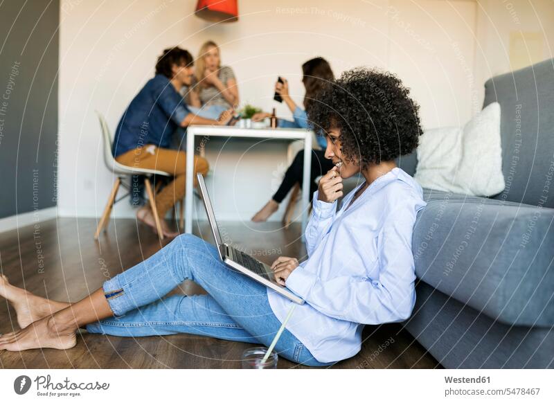 Frau sitzt auf dem Boden mit Laptop mit Freunden im Hintergrund sitzen sitzend Böden Boeden weiblich Frauen Notebook Laptops Notebooks Freundschaft