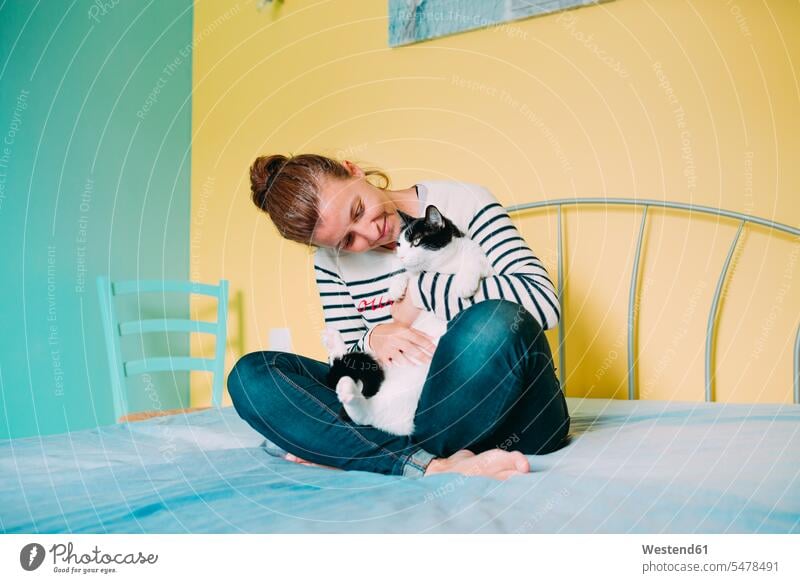Glückliche Frau mit einer schwarz-weißen Katze auf dem Bett Katzen Schmusetier Schmusetiere tierlieb Tierliebe weiblich Frauen Nähe nah innig umarmen Umarmung