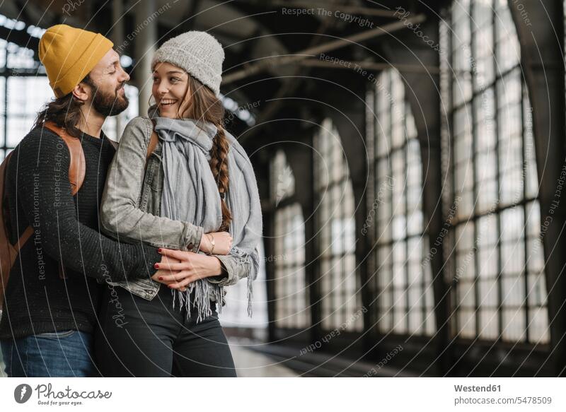 Glückliches junges Paar auf dem Bahnsteig, Berlin, Deutschland Touristen Rucksäcke verreisen Arm umlegen Umarmung Umarmungen Jahreszeiten freuen Frohsinn