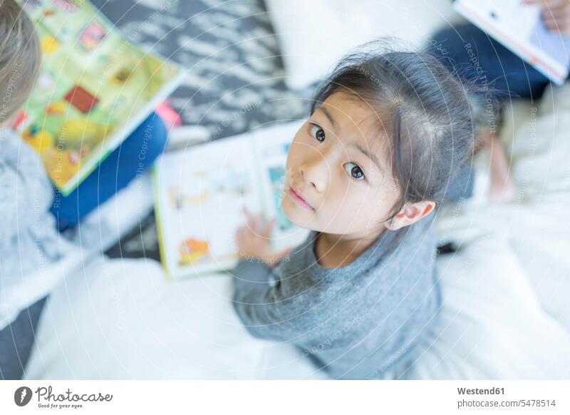 Porträt eines auf dem Boden sitzenden Schulmädchens mit Buch in der Schule Schülerin Portrait Schulkind Bildung Freizeitbeschäftigung Pausenraum Mitschüler