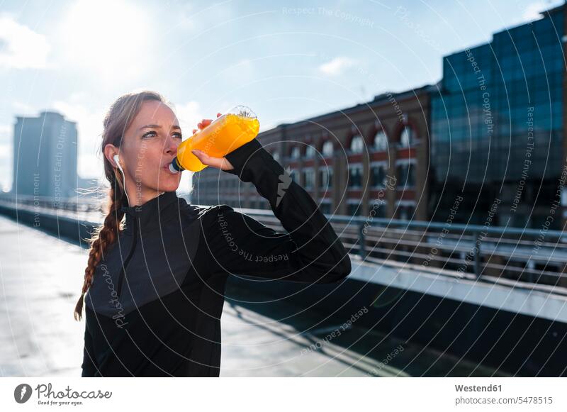 Weibliche Sportlerin trinkt, während sie bei Sonnenschein auf dem Dach gegen den Himmel steht Farbaufnahme Farbe Farbfoto Farbphoto Außenaufnahme außen draußen