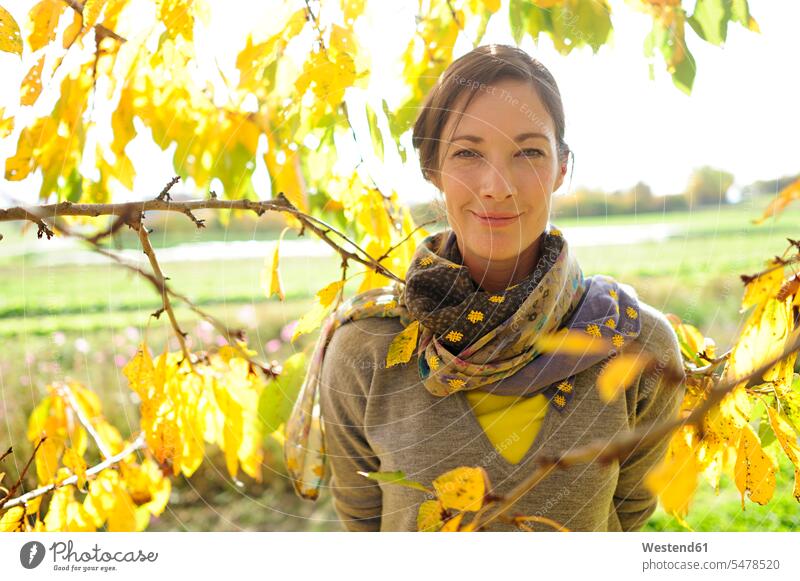 Porträt einer Frau an Zweigen mit Herbstlaub, die in die Kamera schaut Schals freuen geniessen Genuss Glück glücklich sein glücklichsein zufrieden gelbe gelber