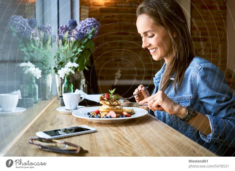 Lächelnde junge Frau isst Pfannkuchen im Cafe essen essend lächeln Kaffeehaus Bistro Cafes Café Cafés Kaffeehäuser weiblich Frauen Pancake Eierkuchen Pancakes