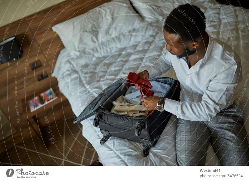 Geschäftsmann sitzt auf dem Bett im Hotelzimmer und packt seinen Koffer geschäftlich Geschäftsleben Geschäftswelt Geschäftsperson Geschäftspersonen Businessmann