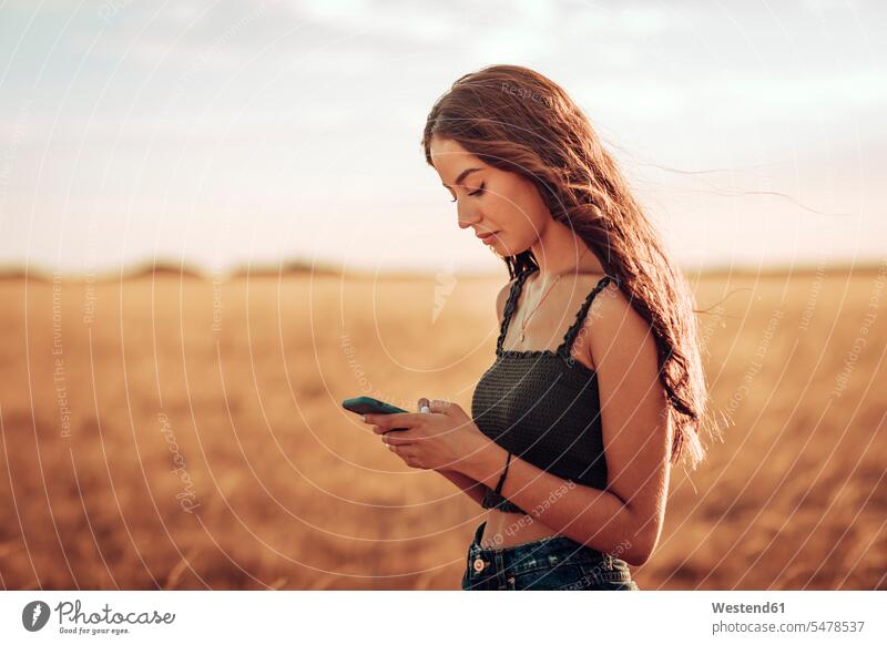 Junge Frau mit langen Haaren benutzt Mobiltelefon, während sie auf Landschaft gegen den Himmel steht Farbaufnahme Farbe Farbfoto Farbphoto Spanien