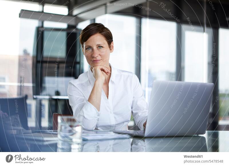 Porträt einer selbstbewussten Geschäftsfrau, die mit Laptop an einem Glastisch im Büro sitzt Zuversicht Zuversichtlich Selbstvertrauen Vertrauen Geschäftsfrauen