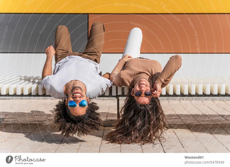 Paar mit Sonnenbrille, auf der Bank entspannen, auf dem Rücken liegend, Köpfe herunterhängen Partner Partnerschaften Bänke Sitzbank Sitzbänke Brillen