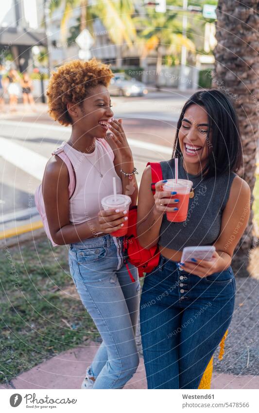 USA, Florida, Miami Beach, zwei glückliche Freundinnen mit Handy und Softdrink in der Stadt Mobiltelefon Handies Handys Mobiltelefone staedtisch städtisch Glück
