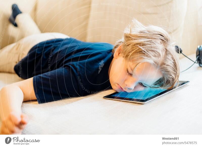 Junge liegt auf Tablette auf Couch und macht ein Nickerchen T-Shirts Couches Liege Sofas Kopfhoerer Telekommunikation Headsets schlafend gelangweilt langweilig