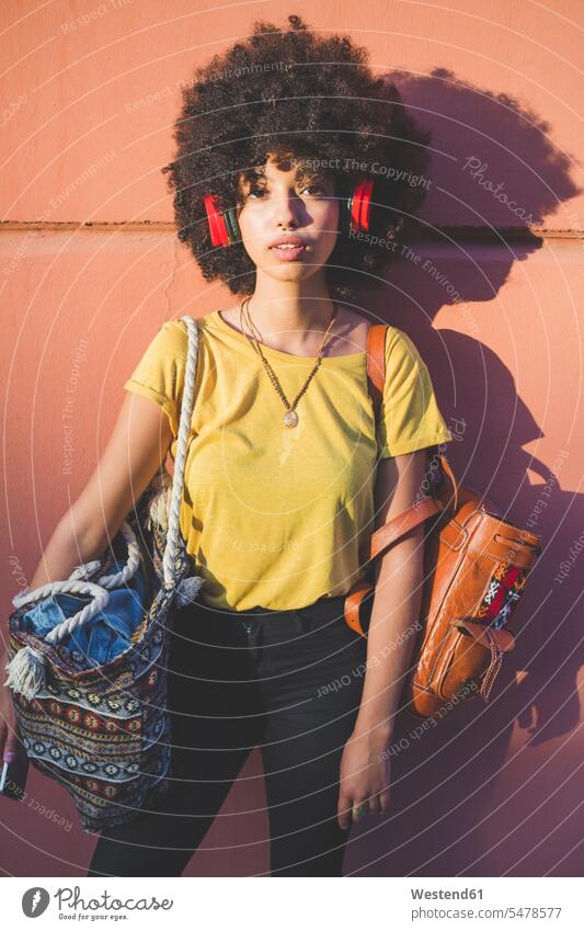 Porträt einer jungen Frau mit Afrofrisur, die mit Kopfhörern Musik hört Leute Menschen People Person Personen gelockt gelockte Haare gelocktes Haar lockig