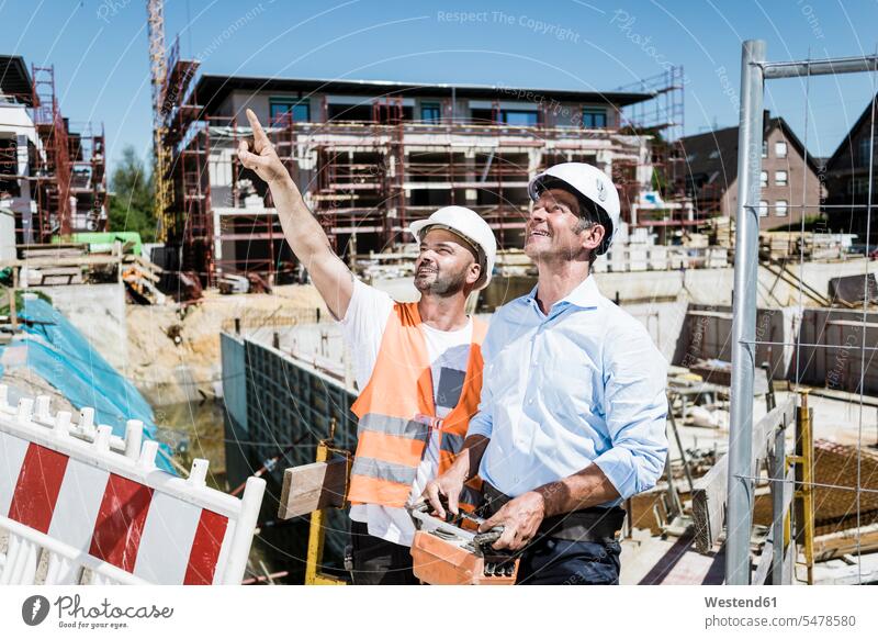 Lächelnder Bauarbeiter im Gespräch mit Mann auf der Baustelle lächeln Männer männlich Baustellen sprechen reden Erwachsener erwachsen Mensch Menschen Leute