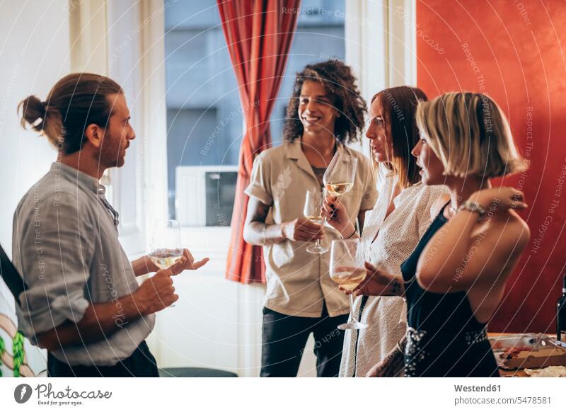 Mann und Frauen hören einem männlichen Freund zu, während sie während der Party Wein trinken Farbaufnahme Farbe Farbfoto Farbphoto Innenaufnahme Innenaufnahmen