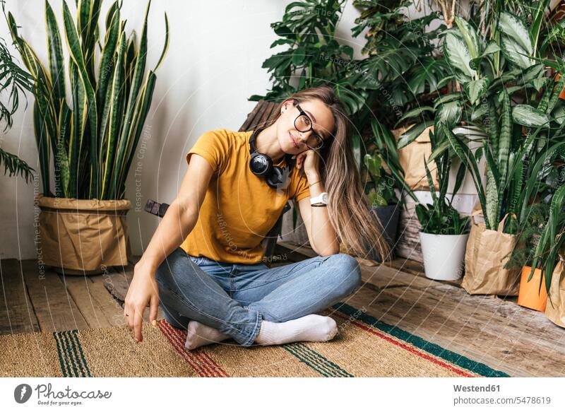 Porträt einer entspannten jungen Frau, die zu Hause auf dem Boden sitzt T-Shirts Kopfhoerer Brillen Teppiche sitzend entspannen relaxen entspanntheit relaxt