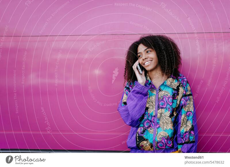 Lächelnde Frau beim Telefonieren, rosa Wand im Hintergrund Jacken Telekommunikation telefonieren Handies Handys Mobiltelefon Mobiltelefone hoeren reden Anruf