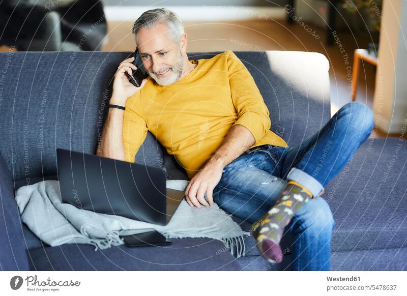 Erwachsener Mann benutzt Handy und Laptop zu Hause auf der Couch Leute Menschen People Person Personen Alleinstehende Alleinstehender Singles Unverheiratete