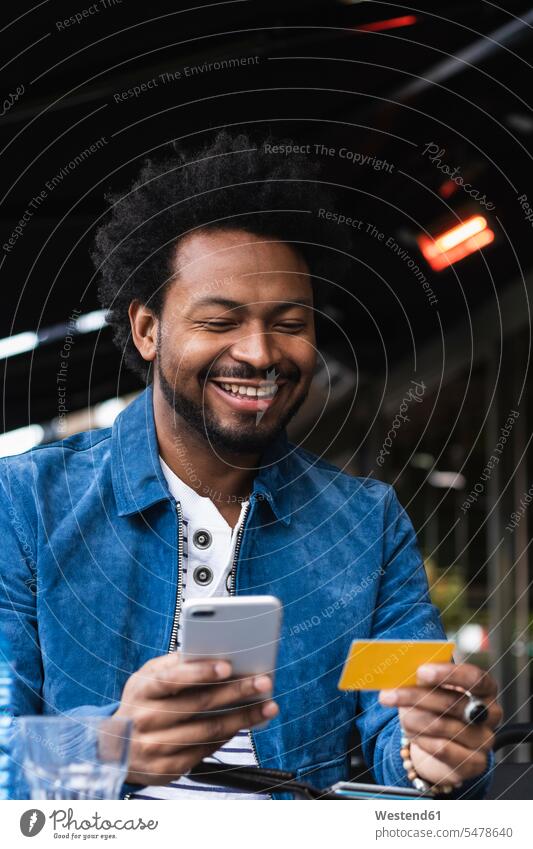 Lächelnder Mann mit Kreditkarte und Smartphone zum Bezahlen im Straßencafé Farbaufnahme Farbe Farbfoto Farbphoto Spanien Freizeitbeschäftigung Muße Zeit