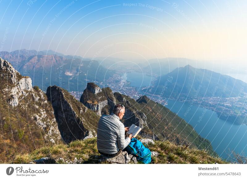 Rückansicht eines Wanderers, der ein Buch auf einem Berggipfel liest, Orobie Alps, Lecco, Italien Leute Menschen People Person Personen Europäisch Kaukasier