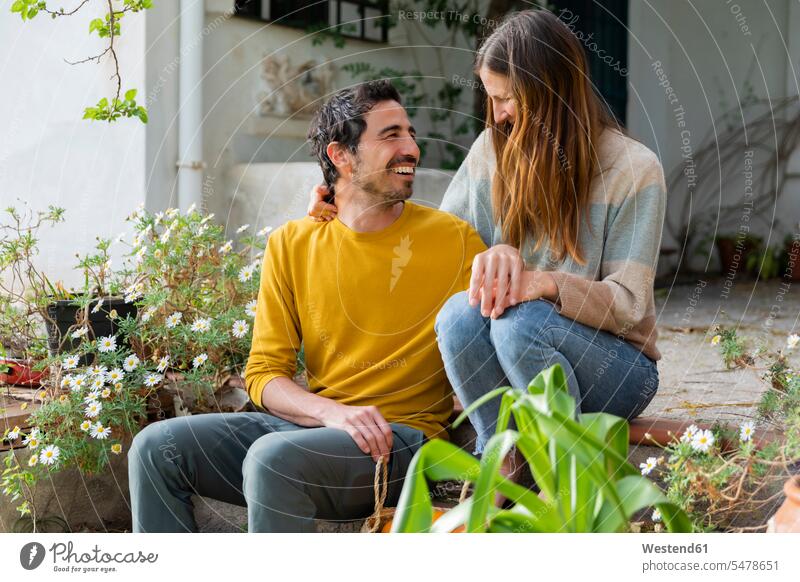 Glückliches Paar unterhält sich, während es auf Stufen gegen das Bauernhaus sitzt Farbaufnahme Farbe Farbfoto Farbphoto Spanien Freizeitbeschäftigung Muße Zeit