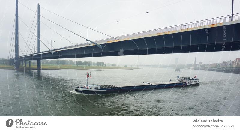 Eine Brücke über den Rhein an einem regnerischen Tag. Ein beladener Lastkahn fährt unter der Brücke hindurch Deutschland grau Himmel Wasser Regen Landschaft
