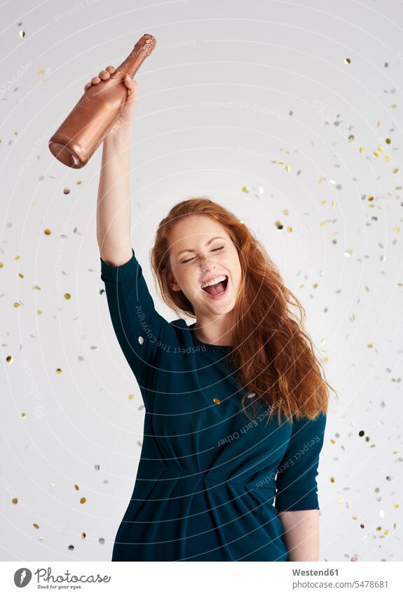 Porträt einer glücklichen jungen Frau mit einer Flasche Champagner beim Konfettiregen Sektflasche Sektflaschen Confetti weiblich Frauen Portrait Porträts