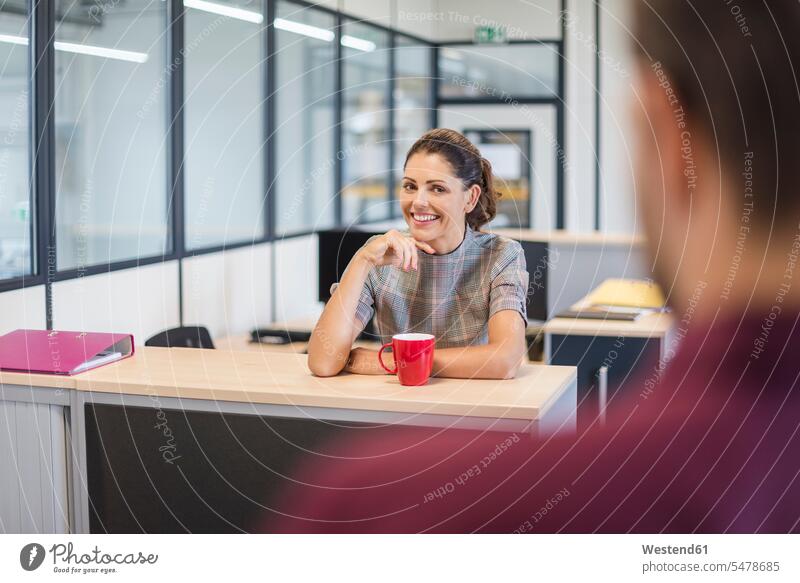 Weibliche Angestellte sitzt am Schreibtisch und spricht mit einem Kollegen sprechen reden Büroangestellte Mitarbeiterin Kollegin Kolleginnen Kaffee sitzen