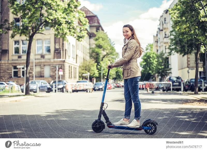 Porträt einer lächelnden Frau mit E-Scooter in der Stadt KFZ Verkehrsmittel Automobil Autos PKW PKWs Wagen freuen zufrieden stehend steht Muße außen draußen