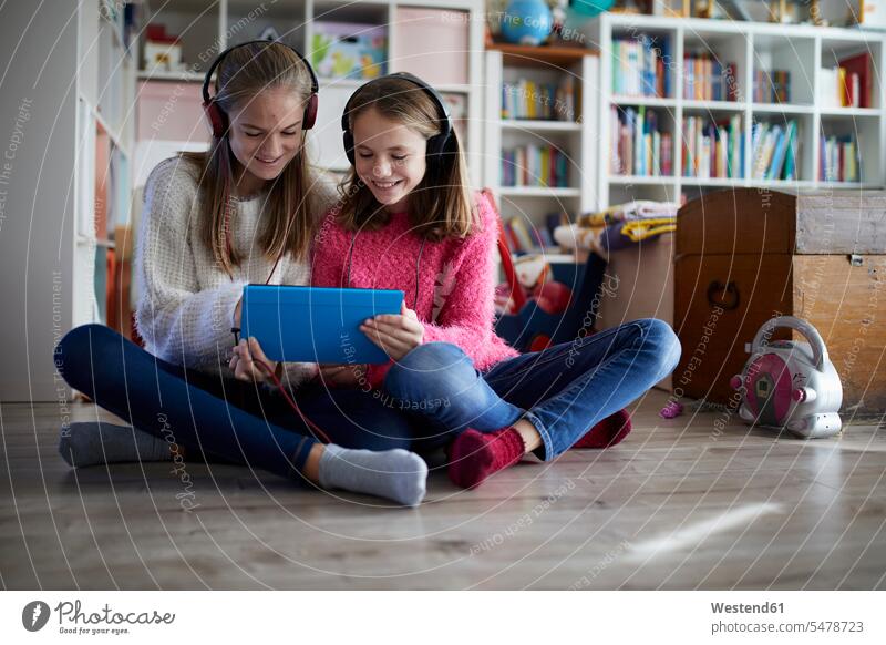 Geschwister spielen zu Hause mit ihren digitalen Tablets, sitzen auf dem Boden Deutschland Kindheit offenes Lächeln lachen offenes Laecheln Gemeinsamkeit