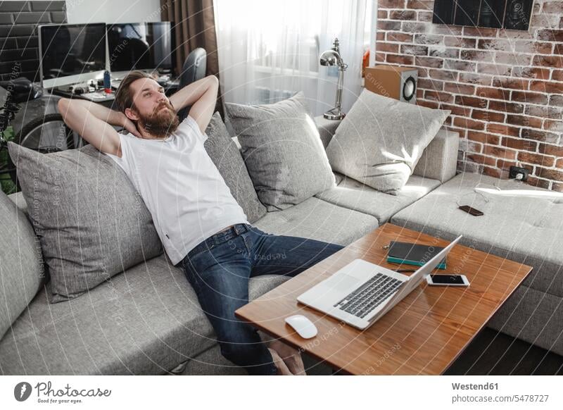 Lächelnder Mann entspannt zu Hause auf der Couch Männer männlich Zuhause daheim Sofa Couches Liege Sofas lächeln Entspannung Entspannen relaxen entspannen