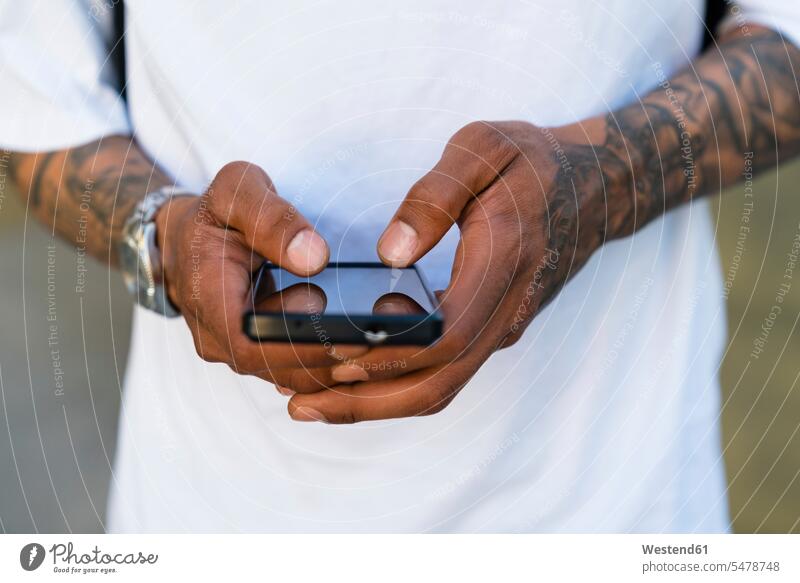Hände eines tätowierten Mannes mit Smartphone, Nahaufnahme T-Shirts Telekommunikation Handies Handys Mobiltelefon Mobiltelefone Displays Farben Farbtoene