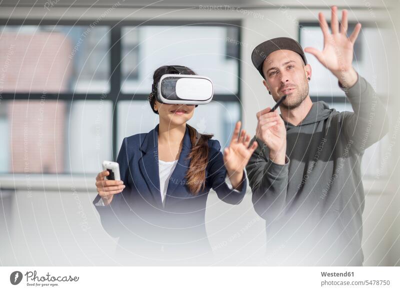 Mann unterrichtet Geschäftsfrau mit VR-Brille im Büro Office Büros Brillen anweisen anleiten Instruktion Anweisung Virtuelle Realität Virtuelle Realitaet Frau