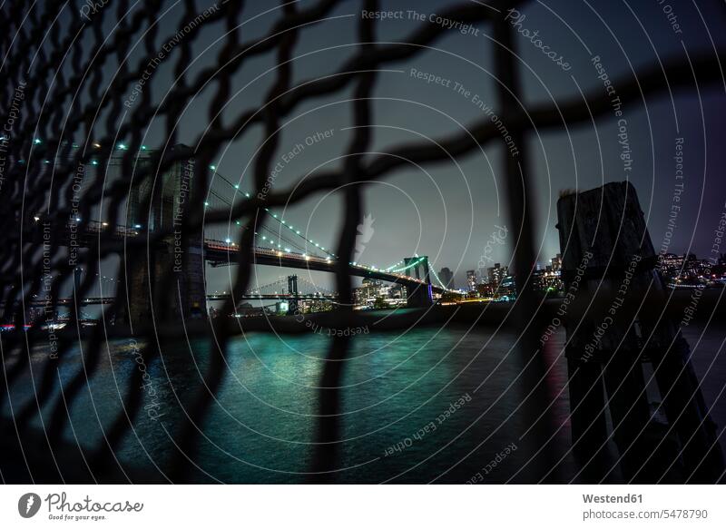 USA, New York, New York City, Kettengliedzaun gegen beleuchtete Brooklyn Bridge bei Nacht Außenaufnahme außen draußen im Freien Langzeitbelichtung Architektur