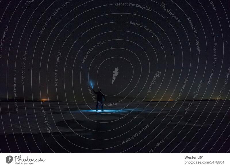 Russland, Amur-Oblast, Silhouette eines Mannes mit Blaustrahl, der nachts unter dem Sternenhimmel auf dem gefrorenen Fluss Zeya steht Seja blau blaue blauer