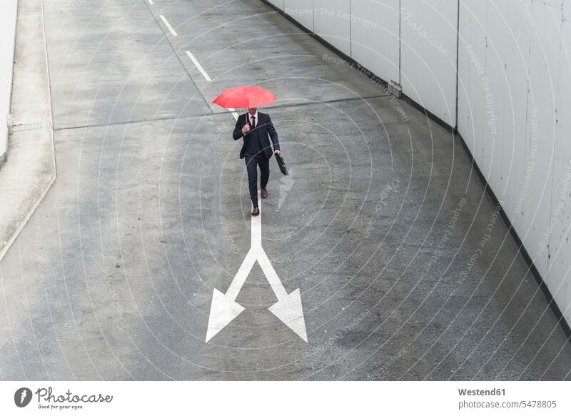 Geschäftsmann mit rotem Regenschirm geht auf Straßenmarkierung Farbaufnahme Farbe Farbfoto Farbphoto Außenaufnahme außen draußen im Freien Tag