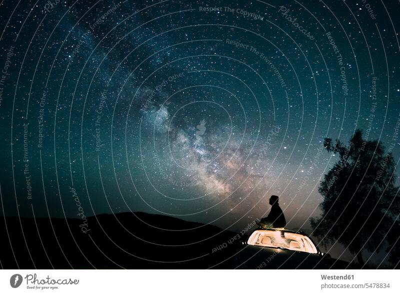 Österreich, Mondsee, Silhouette eines Mannes, der auf einem Autodach unter Sternenhimmel sitzt Sternhimmel betrachten betrachtend Umriß Gegenlicht