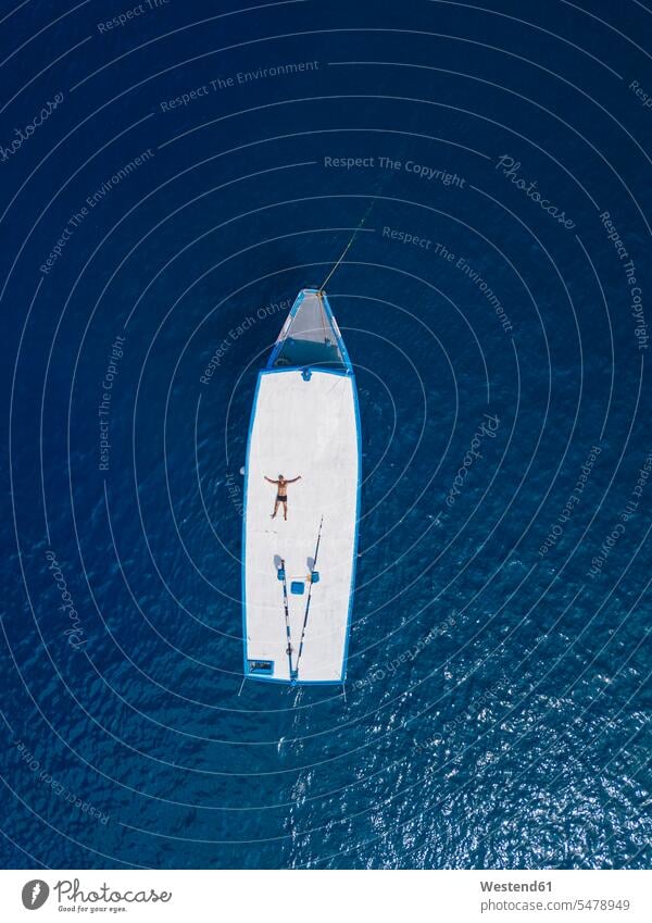 Luftaufnahme eines Mannes ohne Hemd, der sich auf dem Dach eines Bootes entspannt, das im Sommer im blauen Wasser des Arabischen Meeres treibt Außenaufnahme