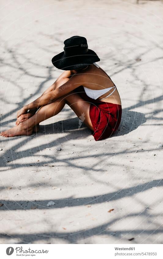 Frau sitzend auf Sand, trägt einen schwarzen Hut Hüte schöne Frau schöne Frauen sandig sitzt schöne Menschen Schön Beauty Schoenheit Schönheit reisen Travel