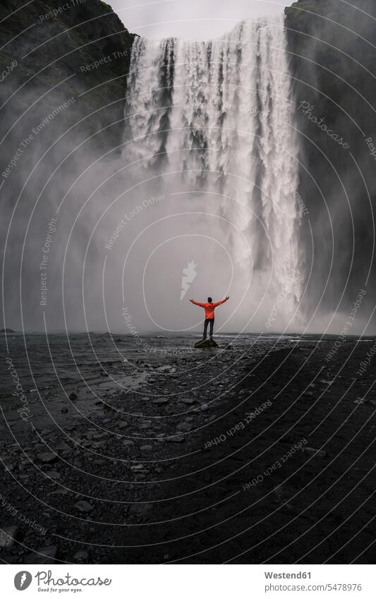 Reifer Mann vor den Skogafoss-Wasserfällen mit erhobenen Armen stehend, Island Jacken frei auf Achse in Bewegung Abenteuer abenteuerlich Landschaften