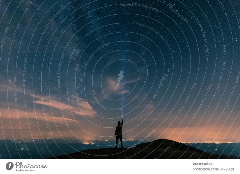Italien, Monte Nerone, Silhouette eines Mannes mit Fackel unter Nachthimmel mit Sternen und Milchstraße Sternenhimmel ansehen Umriß Gegenlicht Schattenbilder