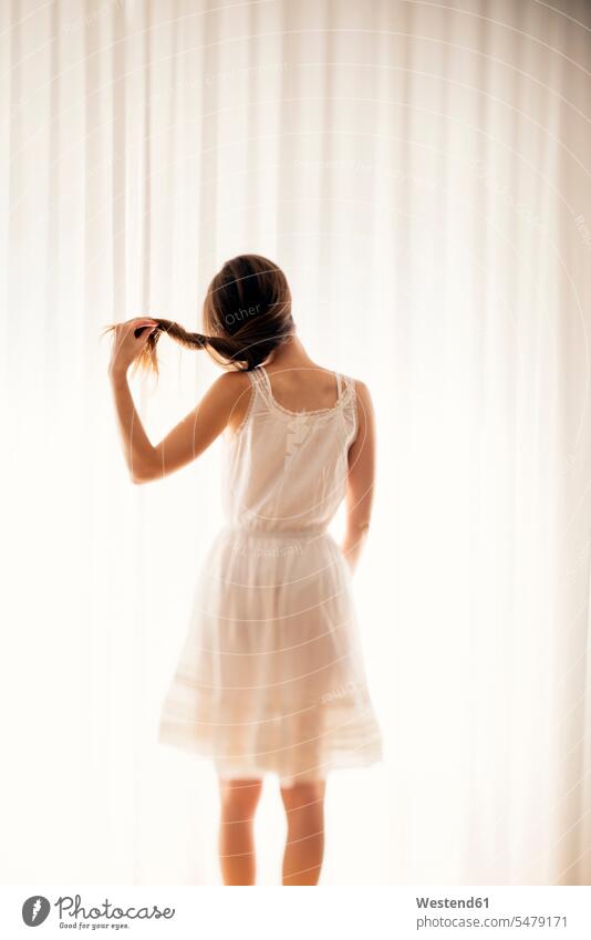Junge Frau spielt mit ihren Haaren vor einem weißen Vorhang, Rückenansicht Gardinen Vorhänge differenzierter Fokus Umriss Kontur drehen Drehung Nur eine Frau 1