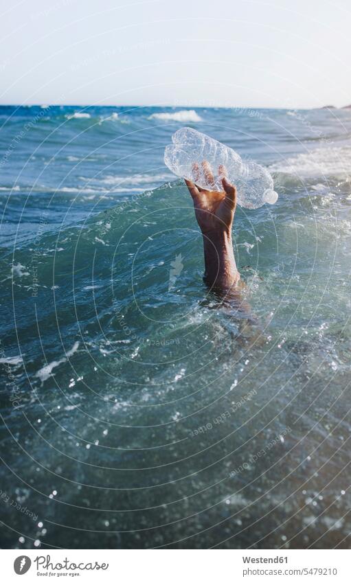 Männerhand hebt Plastikflasche auf leere Abfaelle Abfälle Muell Müll Travel Urlaub Ferien Horizonte Textfreiraum Wellen außen draußen im Freien close up