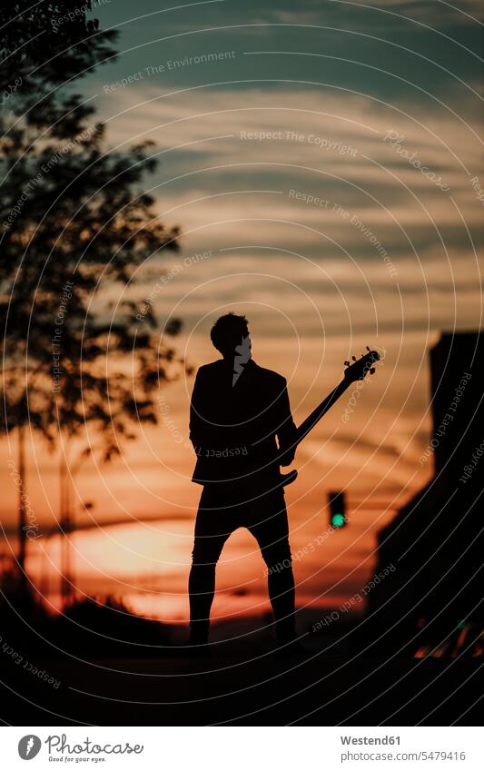 Silhouette eines Musikers, der Bassgitarre spielt, während er auf der Straße steht Farbaufnahme Farbe Farbfoto Farbphoto Außenaufnahme außen draußen im Freien
