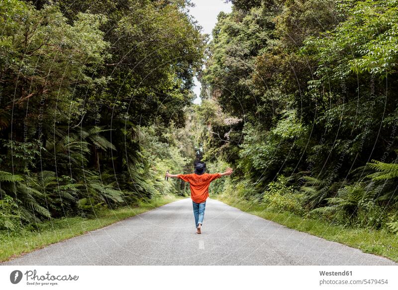 Junger Mann geht mit ausgestreckten Armen auf einer Landstraße im Wald Farbaufnahme Farbe Farbfoto Farbphoto Außenaufnahme außen draußen im Freien Tag