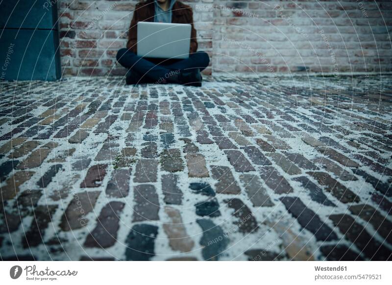 Teenager, der einen Laptop benutzt und auf einem Steinboden in der Stadt sitzt Kriminalitaet Kriminelle Rechner Laptops Notebook Notebooks sitzend abends Muße